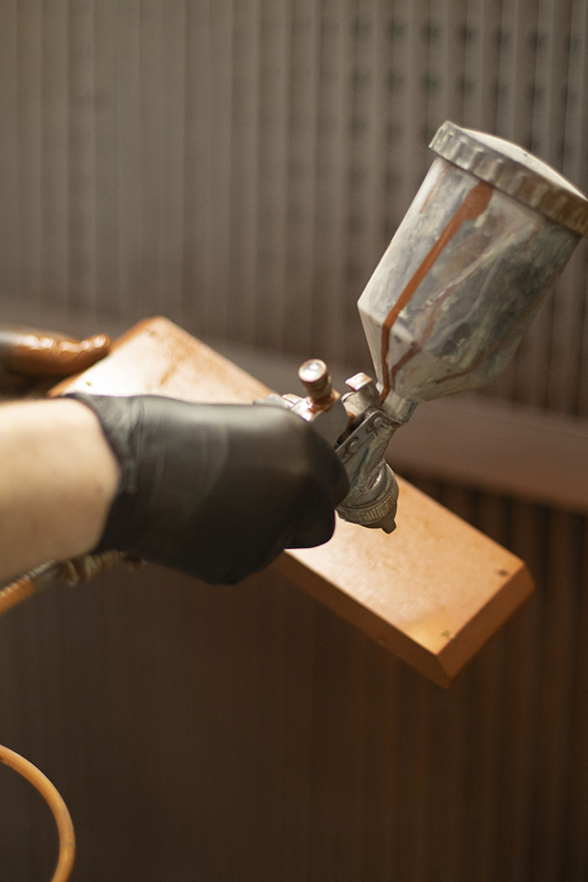 man spraying a piece of wood with clear lacquer