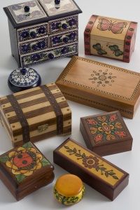 A collection of wooden decorative boxes in various shapes, sizes, and patterns, including floral and butterfly motifs, displayed on a light surface.