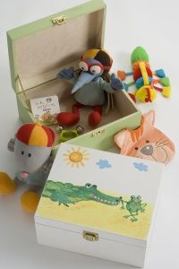 A green toy box with a colourful bird toy inside, surrounded by a mouse plush, a multicoloured rattle, and an orange hippo plush on a white surface.