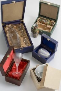Various elegant glassware and ceramics are displayed in open colorfully lined boxes, showcasing a mix of textures and craftsmanship.