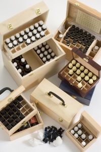 Open wooden boxes filled with rows of small, labelled essential oil bottles. The arrangement suggests organisation and calm, evoking an aromatic atmosphere.