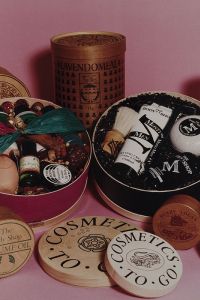 Gift boxes filled with vintage cosmetics and bath products sit on a pink background. Elegant packaging includes ribbons, bottles, and jars, evoking a nostalgic feel.