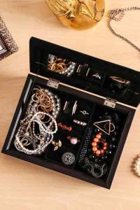 a wooden jewellery box on a table, it is opened and there are a selection of jewellery in it
