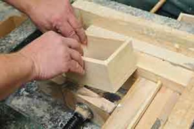 man is putting a glued wooden box into a mitred press